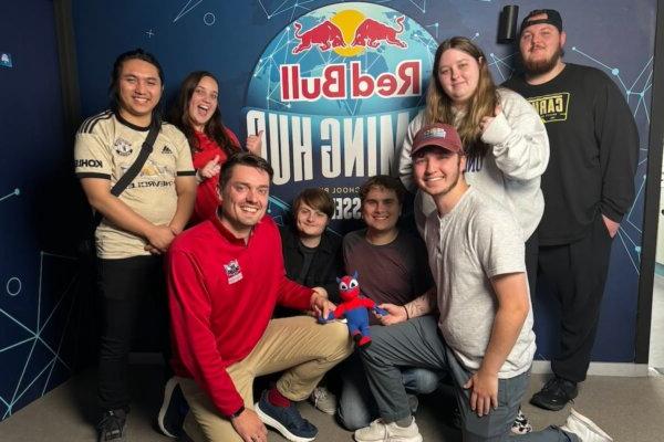 Shenandoah University esports students and staff gathered around a logo (backdrop) for PXL Esports’ Red Bull Gaming Hub in Belgium.